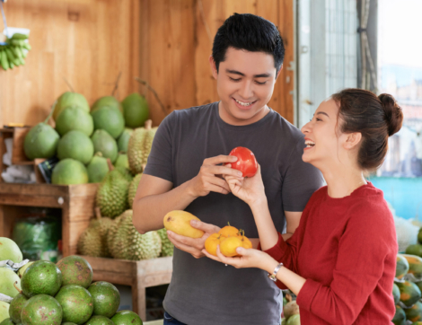 Laughing Vietnamese boyfriend and girlfriend buying ripe fruits and vegetables at market